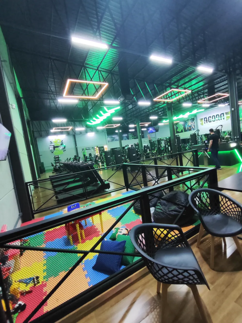 Espaço Kids da Ágora, com tapete colorido e brinquedos, ao lado da área de esteiras